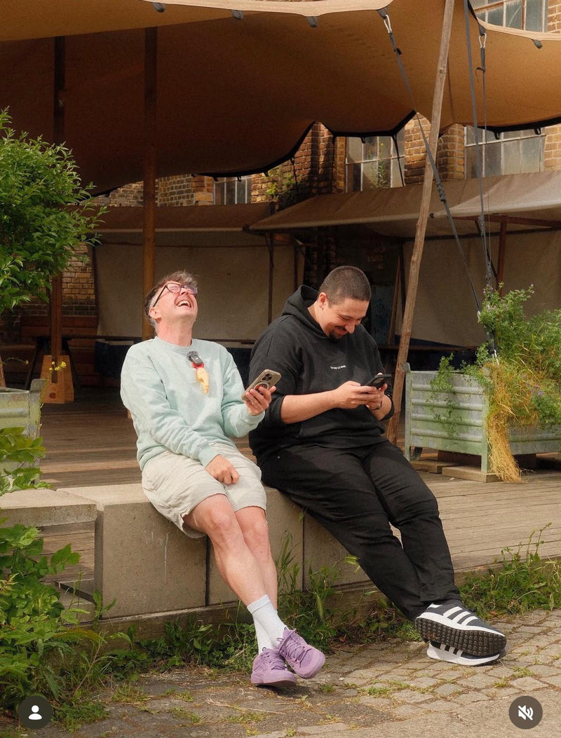 Mikey und Philip vom Cycle Roasters Podcast lachen zusammen auf einer Bank in Lübeck