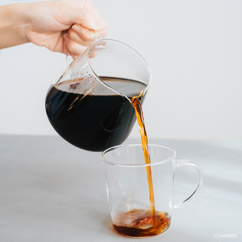 Kaffee wird aus dem Hario V60 Barista Server in eine Glastasse eingeschenkt