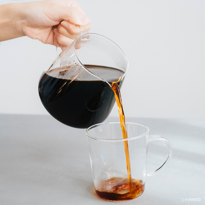 Kaffee wird aus dem Hario V60 Barista Server in eine Glastasse eingeschenkt